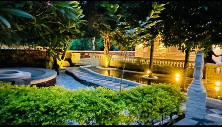 Night view of a landscaped garden with a winding checkered pathway, a small pond, and warm ground lights.
