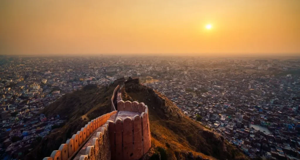 Sunset over a dense city viewed from the ramparts of a historic hilltop fort.