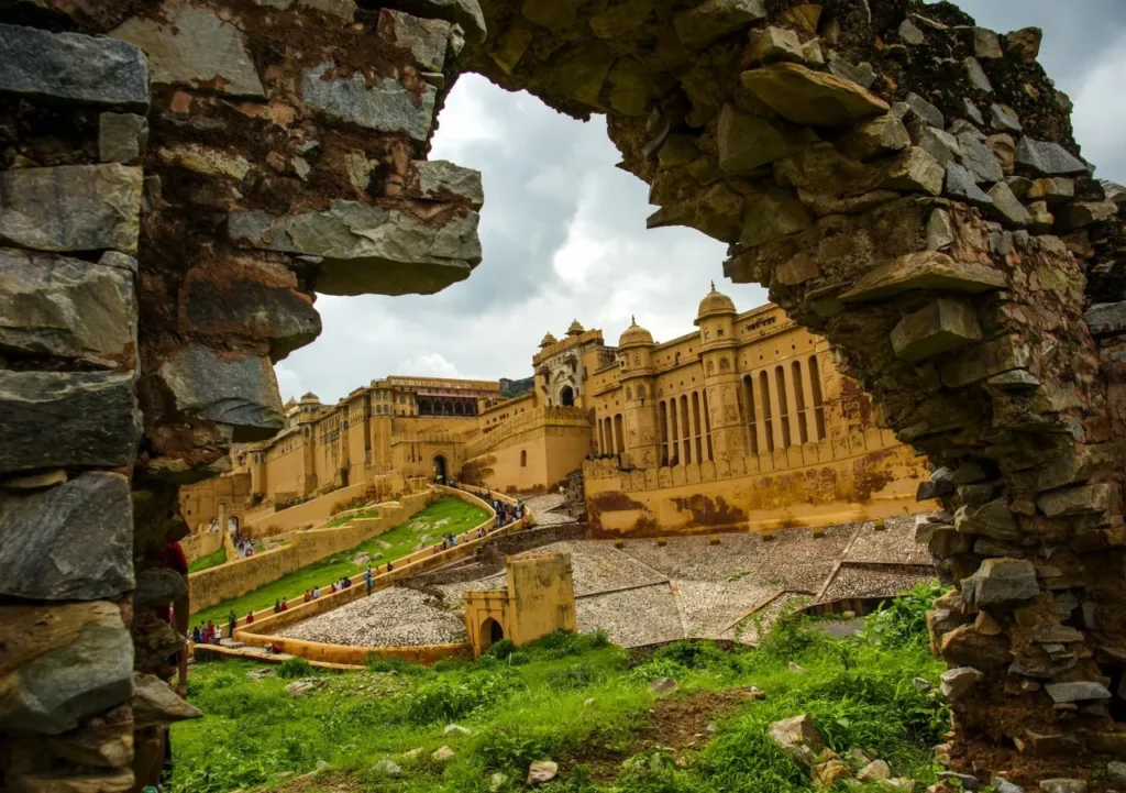 Stone arch framing the Amber Fort with its yellow sandstone walls, courtyards, and arched windows visible beyond; tourists walk along the sloped paths.