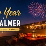 Banner promoting New Year in Jaisalmer with desert camp tents, a crackling fire, camels, and fireworks; ShrINATH Adventures logo in the corner; text reads 'New Year in Jaisalmer' and 'Celebrate. Experience. Remember.'