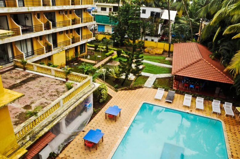Deluxe Room - Peninsula Beach Resort4 - Shrinath Adventures - Desert Camp Jaisalmer A hotel courtyard with a turquoise rectangular pool, sun loungers along the edge, and yellow buildings surrounding a landscaped garden area.