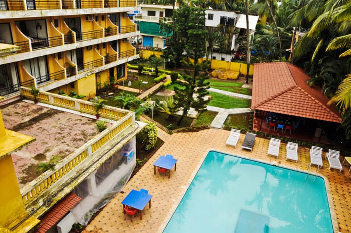 A hotel courtyard with a turquoise rectangular pool, sun loungers along the edge, and yellow buildings surrounding a landscaped garden area.