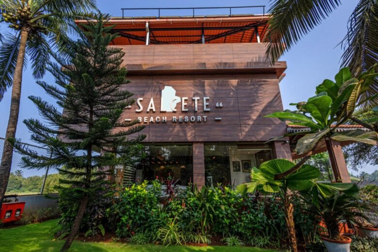 Salcete Beach Resort4 - Shrinath Adventures - Desert Camp Jaisalmer Signage reads Salcete Beach Resort on a brown wooden facade, framed by tropical plants and trees outside the entrance.