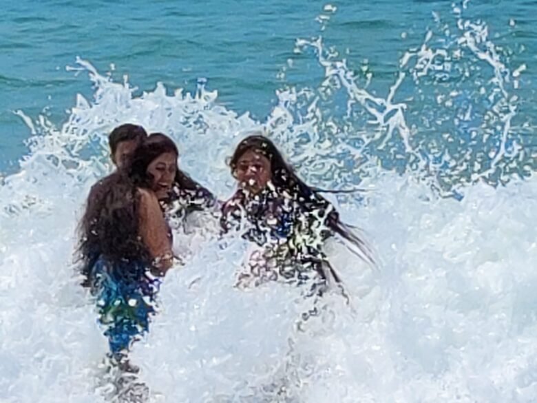 WhatsApp Image 2026-05-28 at 42819 PM - Shrinath Adventures - Desert Camp Jaisalmer Three friends playing in the surf as a big wave crashes around them, smiling and splashing water.