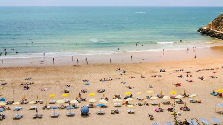 goa tour from rajasthan - Shrinath Adventures - Desert Camp Jaisalmer Busy sandy beach with rows of colorful umbrellas and sun loungers; people swimming and strolling along the turquoise sea.