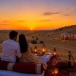 Couple seated on a desert rug at sunset, enjoying a candlelit dinner with lanterns and tents in the background