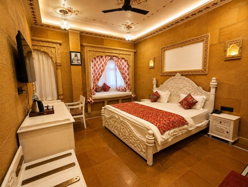 - Shrinath Adventures - Desert Camp Jaisalmer Luxurious Hotel Bedroom with an Ornate White Carved Bed, Red Patterned Runner, and a Window Seating Nook with Curtains.