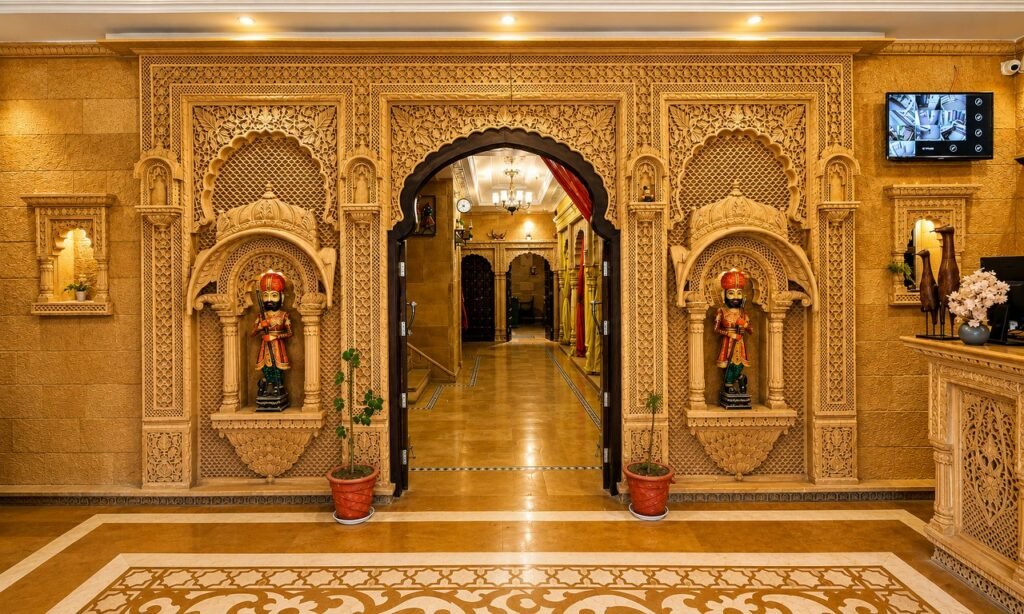 - Shrinath Adventures - Desert Camp Jaisalmer Ornate Hotel Lobby Entrance with Carved Arches and Two Guard Statues in Niches on Either Side of a Central Doorway.