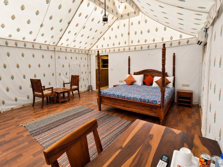 Elegant canvas tent bedroom_1400_1050 - Shrinath Adventures - Desert Camp Jaisalmer - Shrinath Adventures - Desert Camp Jaisalmer Wooden Four-poster Bed with a Blue Patterned Cover and Orange Pillows in a Cream Tent Bedroom.