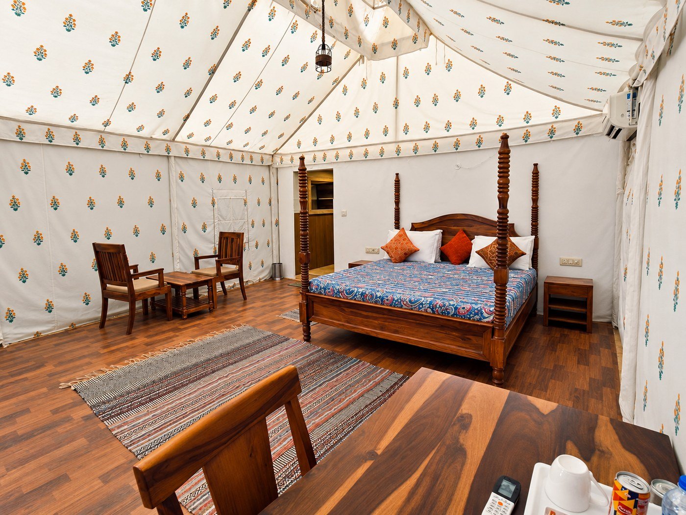 Elegant canvas tent bedroom_1400_1050 - Shrinath Adventures - Desert Camp Jaisalmer - Shrinath Adventures - Desert Camp Jaisalmer Wooden Four-poster Bed with a Blue Patterned Cover and Orange Pillows in a Cream Tent Bedroom.