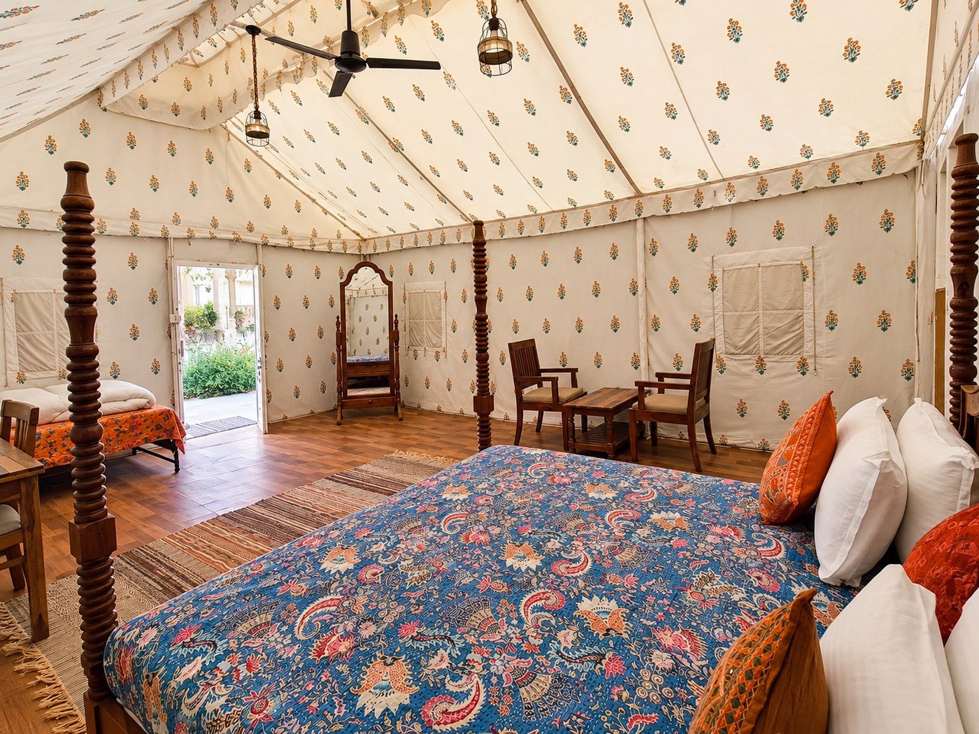 Polished four-poster tent bedroom1_1400_1050 - Shrinath Adventures - Desert Camp Jaisalmer - Shrinath Adventures - Desert Camp Jaisalmer Luxurious Tent Bedroom with a Four-poster Bed, Blue Floral Quilt, Orange Pillows, and Wooden Chairs in a Spacious Interior.